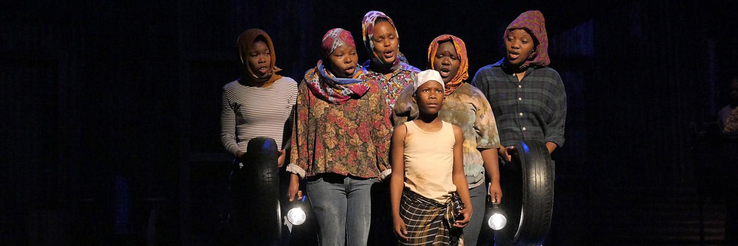Five cast members of Isango Ensemble's A Man of Good Hope stand singing to the child actor on stage at the Young Vic. Photo by Keith Pattison.
