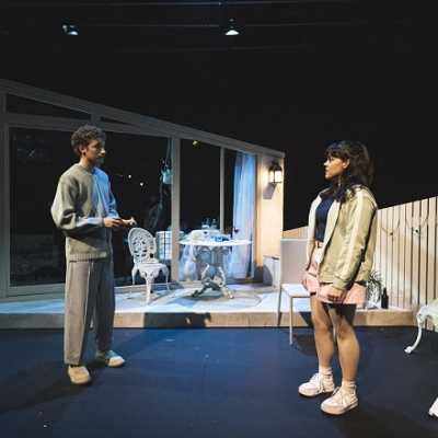 Two people stand speaking to each other in fron of a conservatory set 