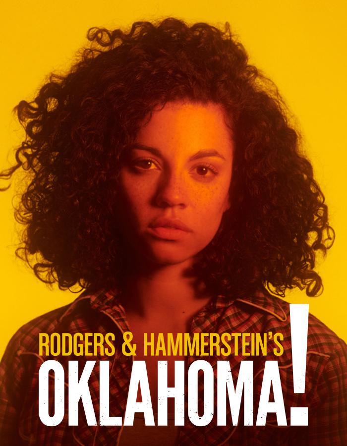 Rodger's & Hammerstein's Oklahoma! From 27th April to 25th June. Image description: A woman with curly hair, wearing a checked shirt, bathed in orange light in front of a yellow background